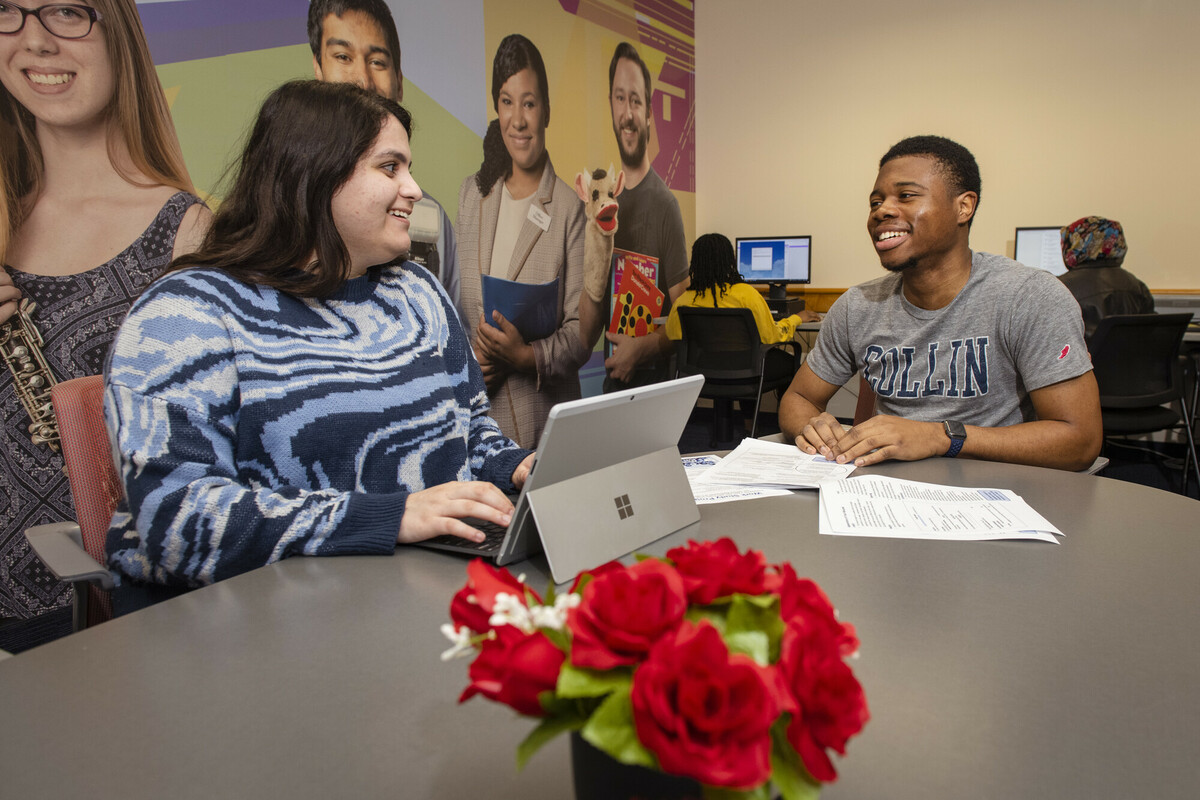 Two students talking and working on a laptop