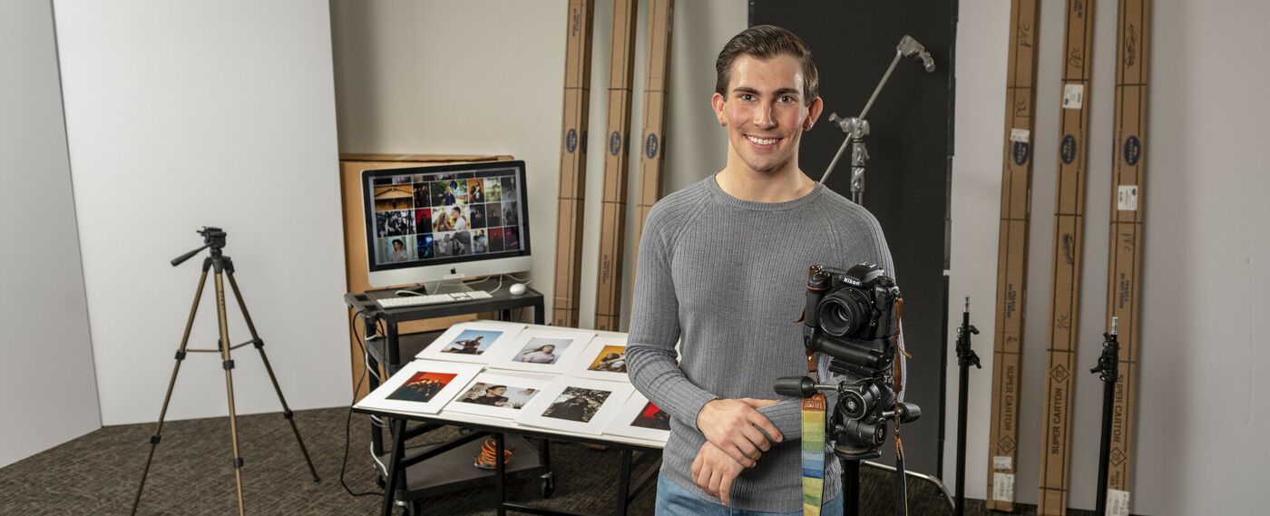 Male student standing with a camera in the photography lab