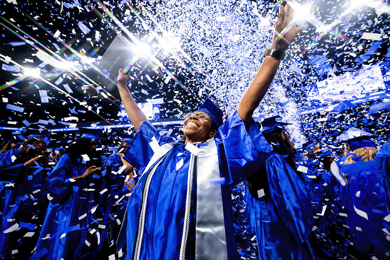A graduate raising their hands up as confetti rains from the venue ceiling