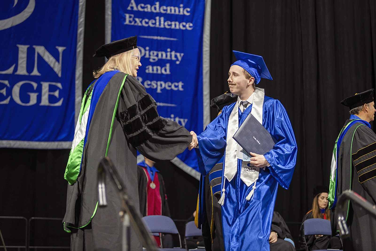 A graduate shaking hands with a professor on stage