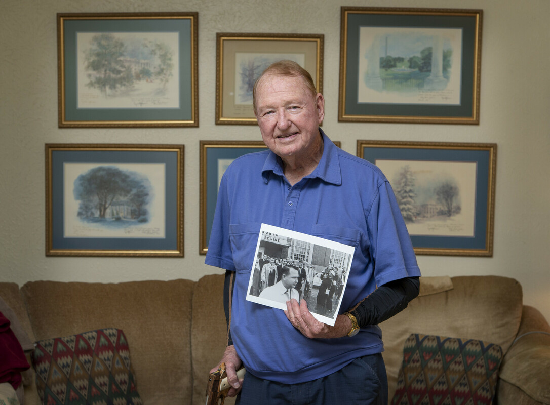 Retired Secret Service agent Mike Howard is photographed in his home in front of framed Christmas cards he received from President Lyndon Baines Johnson (LBJ). The photograph he is holding was taken on the day of President John Fitzgerald Kennedy’s (JFK) assassination and features Howard in the forefront with the president and vice president in the center of the image. Howard teaches Seniors Active In Learning (SAIL) classes at Collin College.