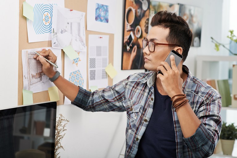 Interior Designer on the phone and writing on a design draft. 
