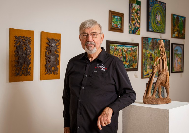 Glenn Stokes of Stokes Art Gallery standing in front of a collection of Haitian art pieces at the Arts Gallery at Collin College on the Plano Campus.